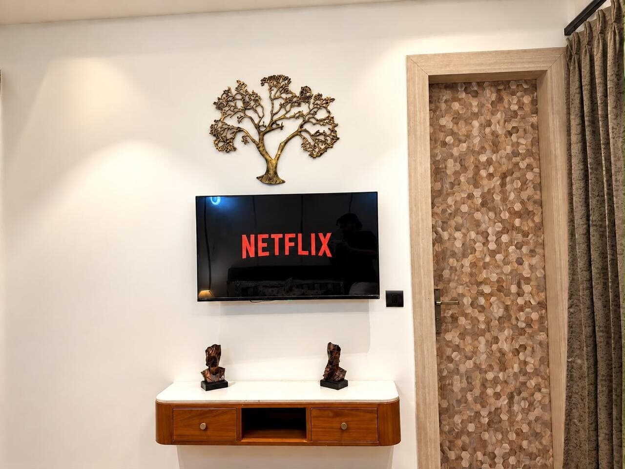 Bedroom wall with a smart TV above a floating walnut console beneath a brass tree-of-life sculpture