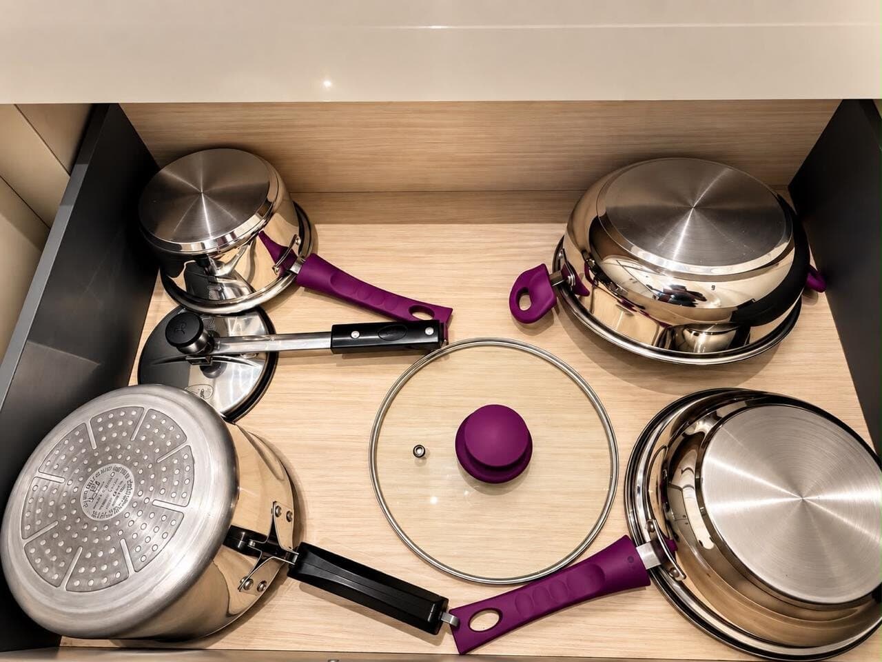 Drawer of stainless-steel cookware — pans, a pressure cooker, and a kadhai with lids