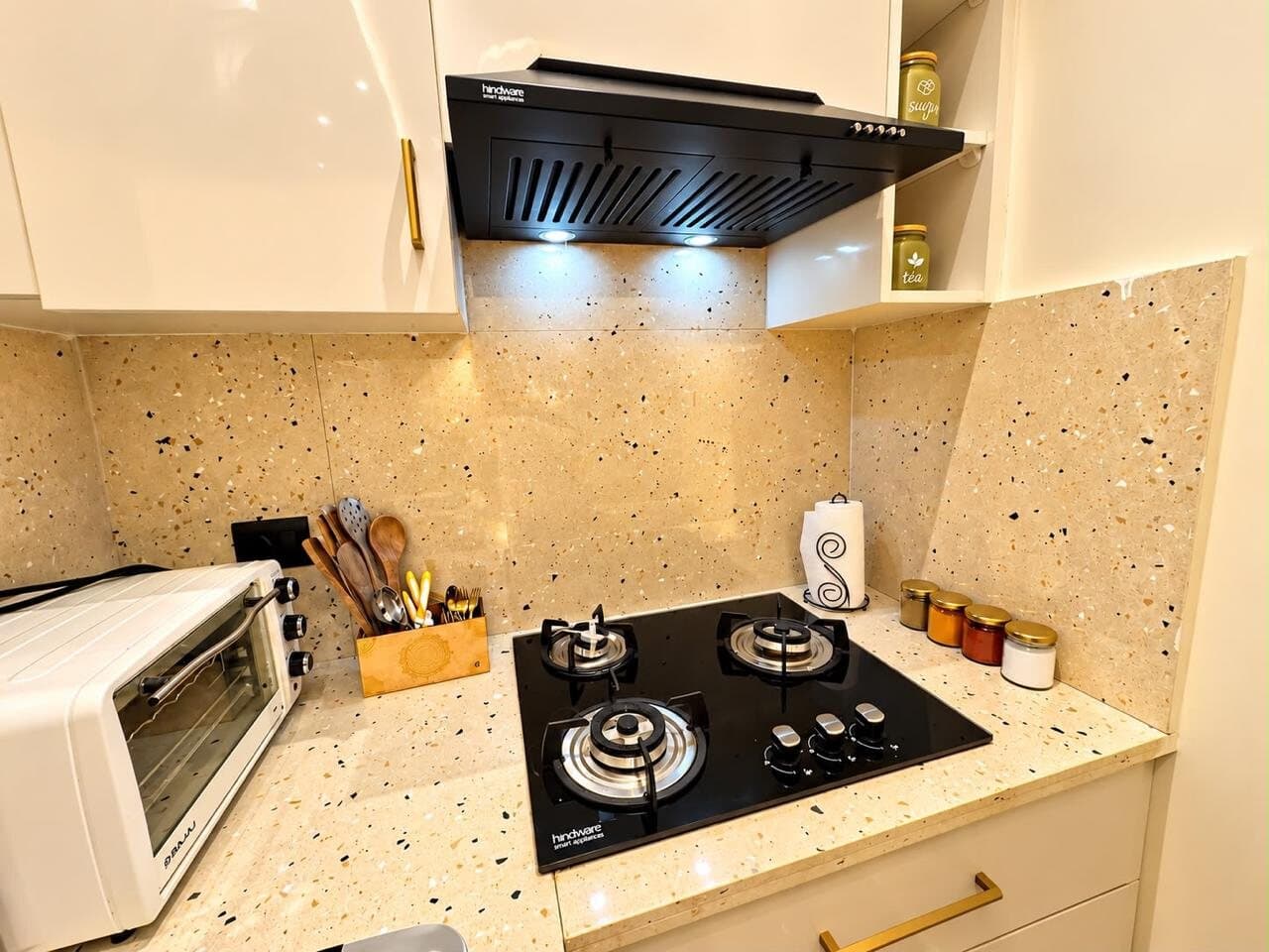 Terrazzo kitchen counter with a three-burner glass hob, oven, chimney hood, and a caddy of wooden utensils