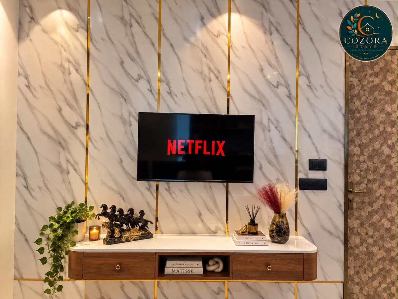 Marble-look TV wall with gold inlay strips, a floating walnut console, horse sculptures, and a trailing pothos